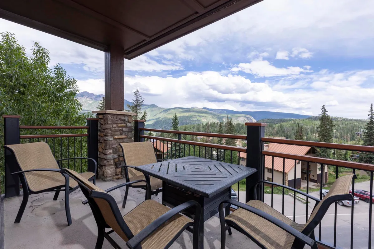A private balcony with patio furniture overlooks a breathtaking mountain view framed by sturdy railings, offering a tranquil spot for relaxation, socializing, or simply soaking in the scenery.