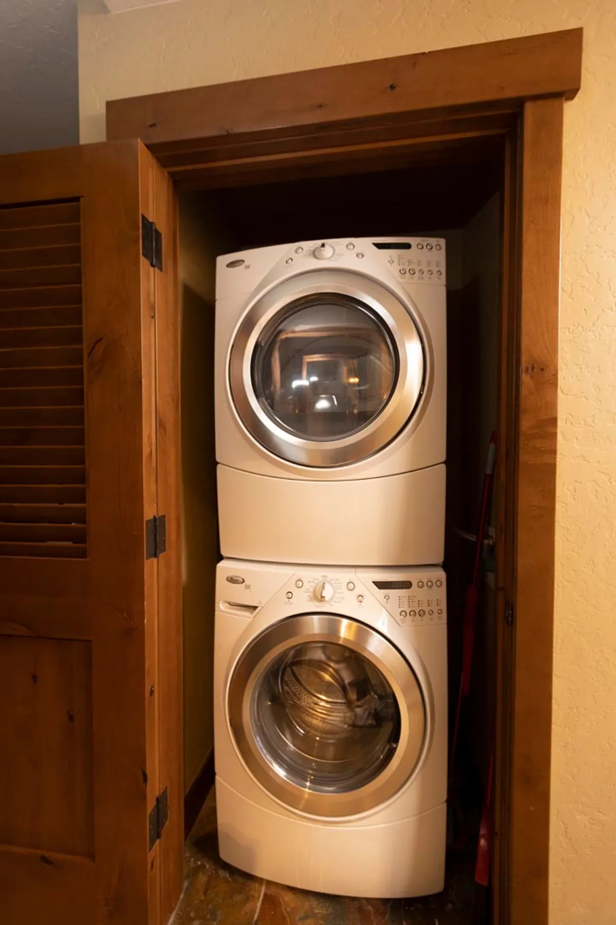 A dedicated laundry area is shown with a stacked washer and dryer, wooden door, and textured wall, conveying efficiency and added convenience for guests during longer stays.