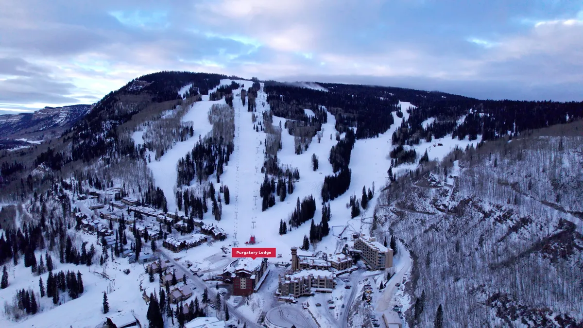 A stunning view of Purgatory Lodge nestled at the base of ski slopes, surrounded by snow-covered mountains and trees. The image captures the essence of ski-in/ski-out convenience with the lodge’s proximity to the action and the breathtaking alpine setting.