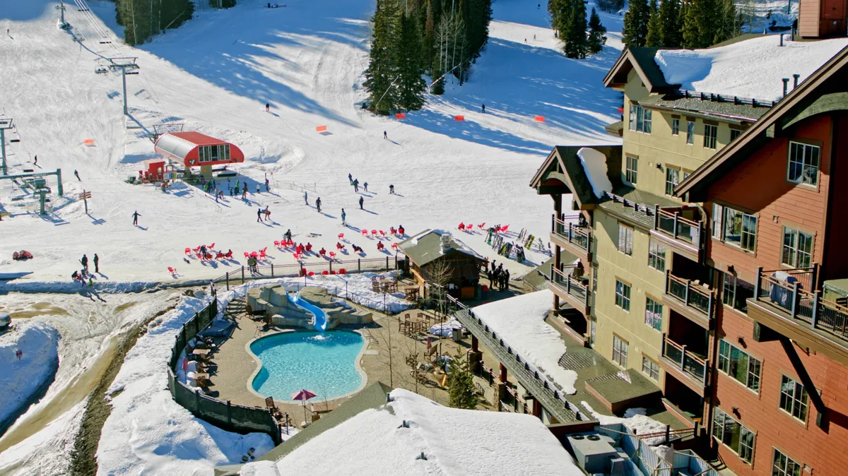 This image captures the pool area adjacent to the ski slopes, featuring guests relaxing in the heated swimming pool with the lodge, ski lifts, and snow-covered scenery in view. The atmosphere is lively and adventurous, emphasizing the blend of recreation and relaxation.