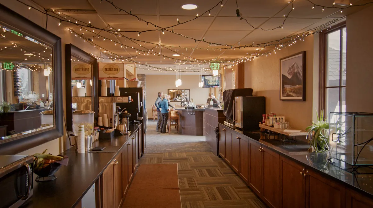 Inside the lodge, a cozy bar area and coffee station offer seating and warm lighting, inviting guests to socialize, relax, or enjoy refreshments in a communal setting.