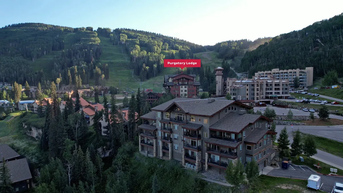 An exterior view of Purgatory Lodge with the surrounding mountains and nearby village buildings. The parking area and lodge exterior create a sense of arrival, while the landscape offers an inviting perspective on the resort environment.