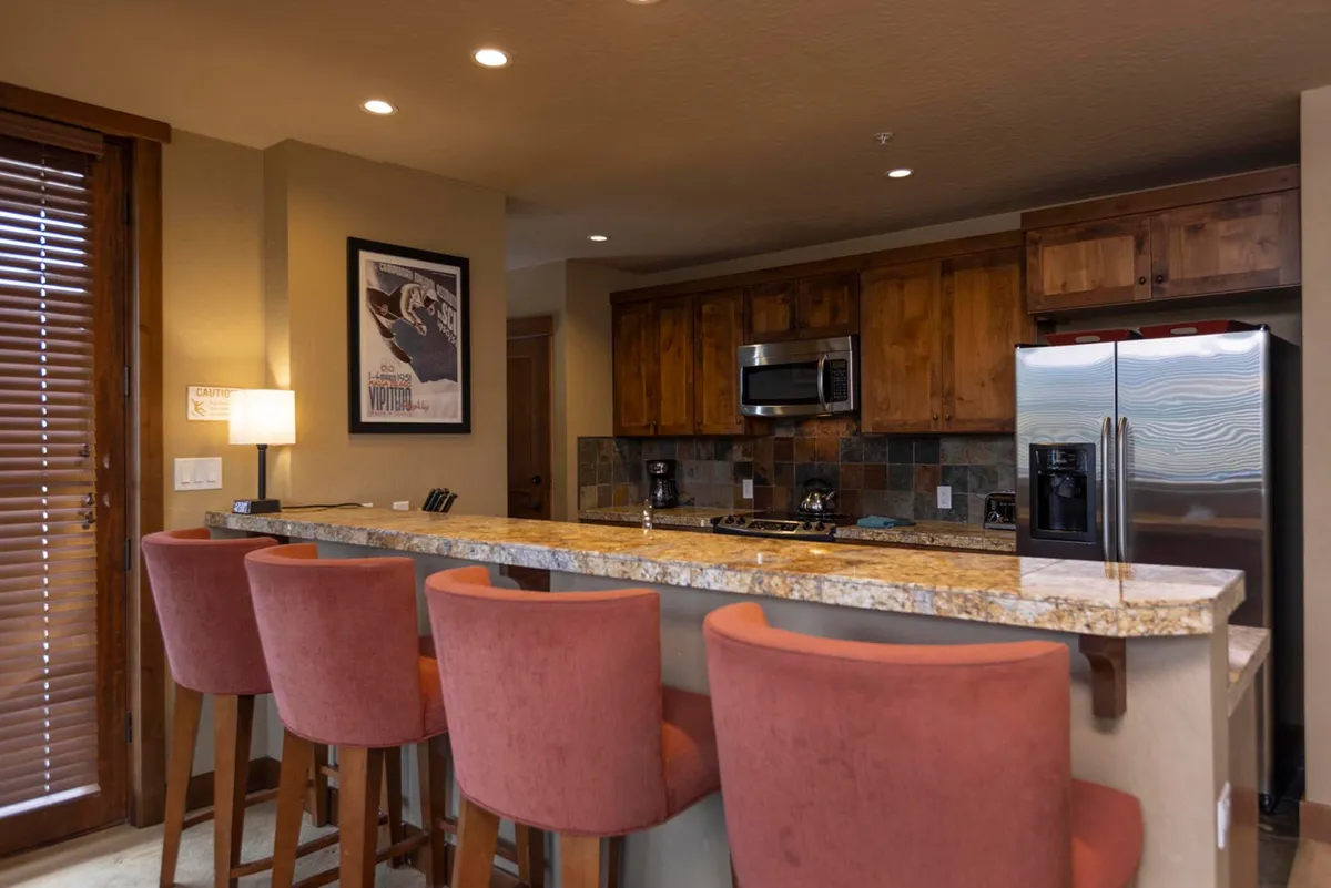A modern, well-equipped kitchen with granite countertops, stainless steel appliances, wood cabinetry, and colorful bar stools, all in an open layout that encourages socializing and culinary activity.