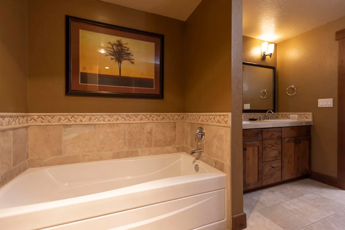 This tranquil bathroom features a spacious bathtub set against wooden cabinetry and accented by framed artwork. The setting is peaceful, designed for long, restorative soaks and quiet moments of self-care amidst a calming backdrop.